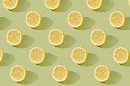 A hard light pattern of a half of a lemon on a pastel green seamless surfaceの写真素材