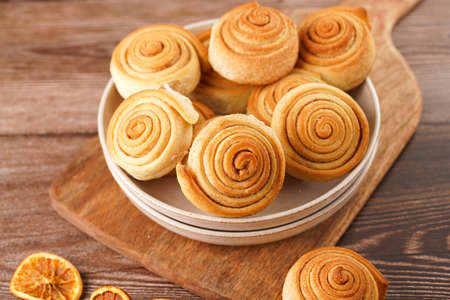 Several cinnamon buns in a beige bowl on wooden board on wooden tableの写真素材