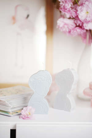 Two gray and blue candles shaped as greek goddess on a white furniture surrounded by pink blossom, close upの写真素材
