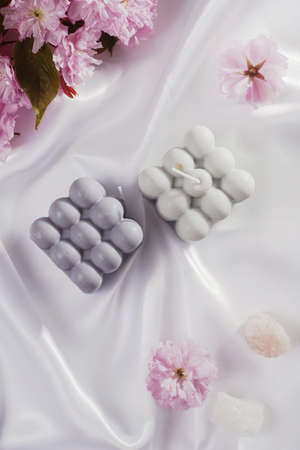 A gray-blue bubble candle on a white silky fabric and pink cherry blossom in the background, top viewの写真素材