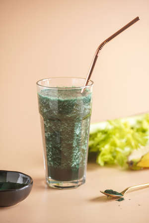 A glass of green healthy detox smoothie with vegetables and spirulina powder and a brass strawの写真素材
