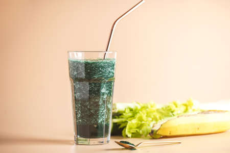 A glass of green healthy detox smoothie with vegetables and spirulina powder and a brass straw