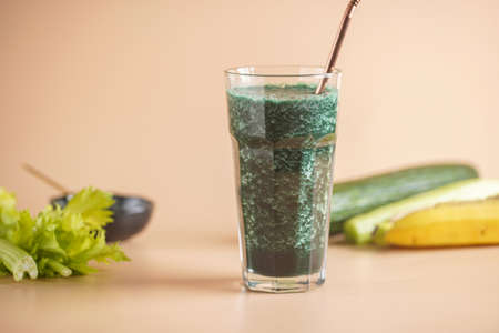 A glass of green healthy detox smoothie with vegetables and spirulina powder and a brass strawの写真素材