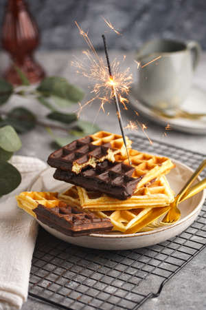 Breakfast waffles with chocolate with golden silverware on gray surface and a sparkler burningの写真素材