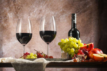 Two glasses of red wine, a bottle of wine and fruit selection: apples, grapes, pomegranate. Still lifeの写真素材