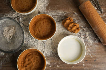 Several small baking forms with dough, flour and rolling pin on a kitchen tableの写真素材