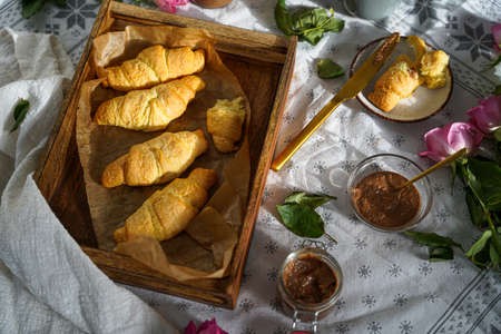 Several butter croissant in a wooden tray on a white table cloth and several jars with jam and butter spread, breakfastの写真素材