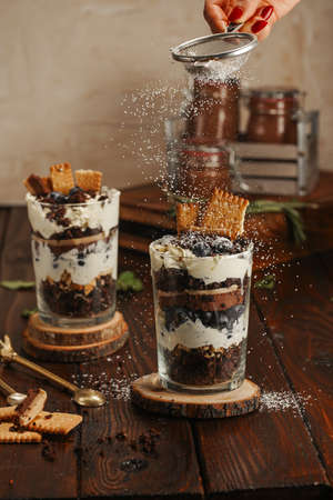 Sifting powdered sugar over two glasses with a layered dessert trifle with chocolate, cream, cookies and blueberriesの写真素材