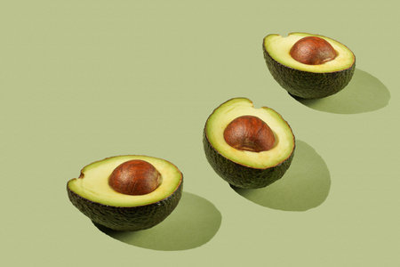 Three avocado halves on a pastel green background
