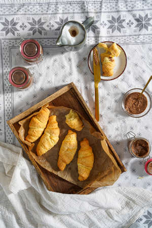 Several butter croissant in a wooden tray on a white table cloth and several jars with jam and butter spread, breakfastの写真素材