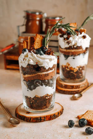 Two glasses with a layered dessert trifle with chocolate, cream, cookies and blueberriesの写真素材