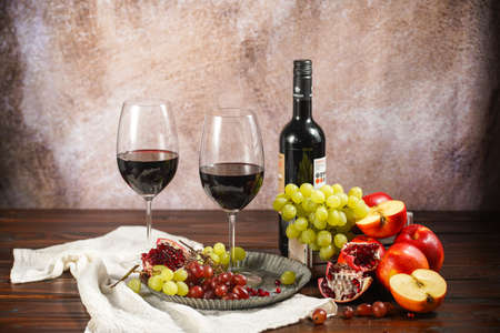 Two glasses of red wine, a bottle of wine and fruit selection: apples, grapes, pomegranate. Still lifeの写真素材