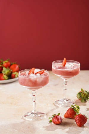 Two glasses with red strawberry dessert with ice cubes and crashed ice and strawberry slices on burgundy backgroundの写真素材