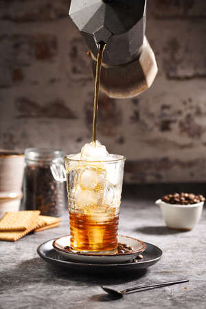 Pouring coffee from moka espresso maker into a glass with ice cubesの写真素材