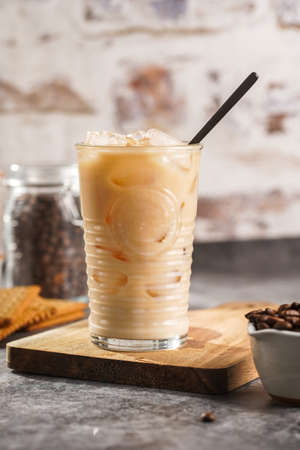 A glass with ice cubes and milk coffee on a wooden boardの写真素材