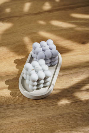 Two gray-blue bubble candles on a concrete tray on a wooden surface in hard lightの写真素材