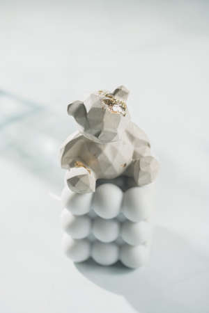 A gray concrete figurine of a teddy bear on a blue bubble candle on pastel blue background