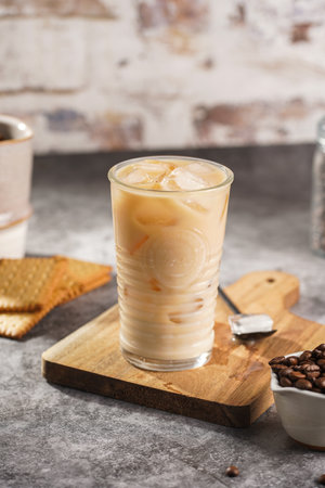 A glass with ice cubes and milk coffee on a wooden boardの写真素材