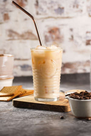 A glass with ice cubes and milk coffee on a wooden board, with brass strawの写真素材
