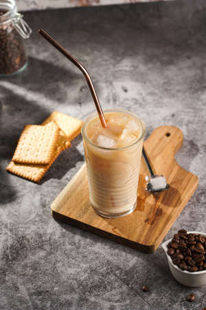 A glass with ice cubes and milk coffee on a wooden board, with brass strawの写真素材