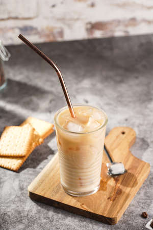 A glass with ice cubes and milk coffee on a wooden board, with brass strawの写真素材