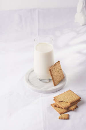 A glass of milk on a marble plate on a white table cloth and freshly baked cookiesの写真素材
