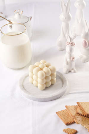One white bubble candle on white table cloth, surrounded by milk and easter bunny figurinesの写真素材