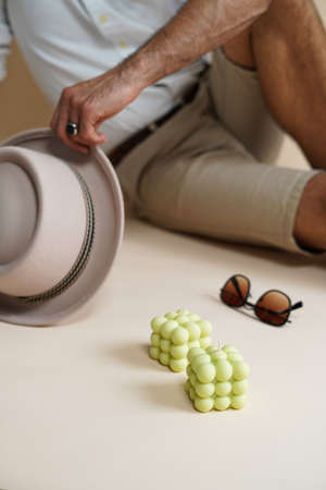 A pastel green bubble candle on an beige colored seamless background, sunglasses, a hat, and a male in the backgroundの写真素材