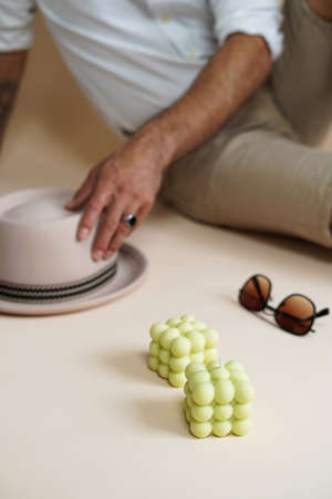 A pastel green bubble candle on an beige colored seamless background, sunglasses, a hat, and a male in the backgroundの写真素材