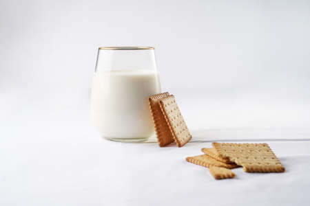 A glass of milk on the white table cloth and freshly baked cookies leaning on the glassの写真素材