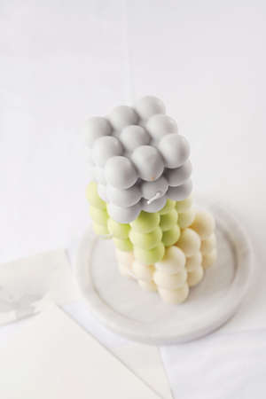 Several bubble candles, gray, patel green and beige stacked on top of each other on white table clothの写真素材