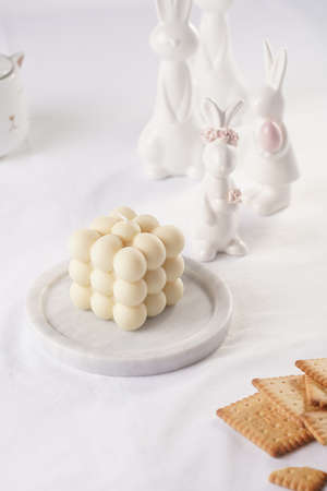 One white bubble candle on white table cloth, surrounded by easter bunny figurinesの写真素材