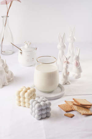 A glass of milk on a marble plate on a white table cloth, freshly baked cookies, bubble candles and white easter bunnies, figurinesの写真素材
