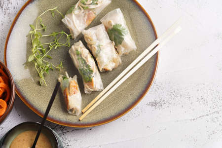 Several spring rolls with chicken, carrot and bamboo sprouts in rice paper on green plate, sesame...