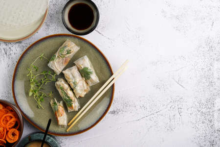 Several spring rolls with chicken, carrot and bamboo sprouts in rice paper on green plate, sesame sauce and coriander on concrete surface. Top view, negative spaceの写真素材