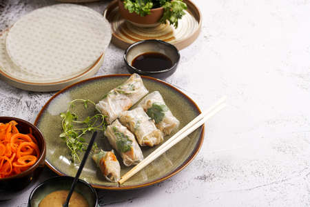 Several spring rolls with chicken, carrot and bamboo sprouts in rice paper on green plate, sesame sauce and coriander on concrete surface. With negative spaceの写真素材