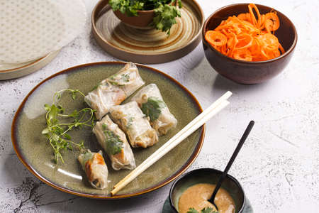 Several spring rolls with chicken, carrot and bamboo sprouts in rice paper on green plate, sesame sauce and coriander on concrete surfaceの写真素材