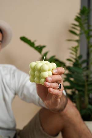 A male hand showing a pastel green bubble candle with a zamioculcas plant in the backgroundの写真素材