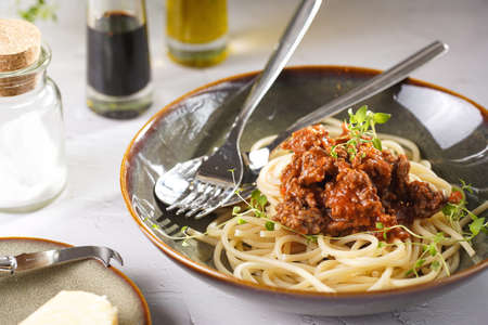 Italian spaghetti with bolognese tomato sauce and fresh thyme in dark green bowl on white concrete surface, with olive oil and balsamic vinegar in the backの写真素材