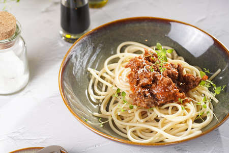 Italian spaghetti with bolognese tomato sauce and fresh thyme in dark green bowl on white concrete surface, with olive oil and balsamic vinegar in the backの写真素材