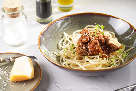 Italian spaghetti with bolognese tomato sauce and fresh thyme in dark green bowl on white concrete surface, with olive oil and balsamic vinegar in the backの写真素材