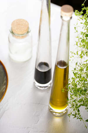 Italian salad dressing ingredients: olive oil, balsamic vinegar, sea salt, thyme and parmesan on white concrete surfaceの写真素材
