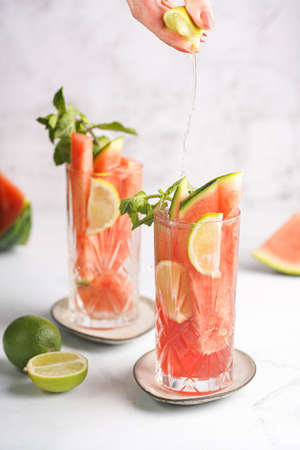 Two glasses with tall long drink with watermelon, lime slices and mint - a hand pressing lime juiceの写真素材
