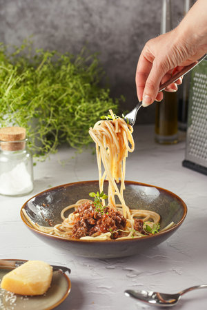 A hand holding a fork with spaghetti with bolognese meat tomato sauce in green bowl garnished with thymeの写真素材