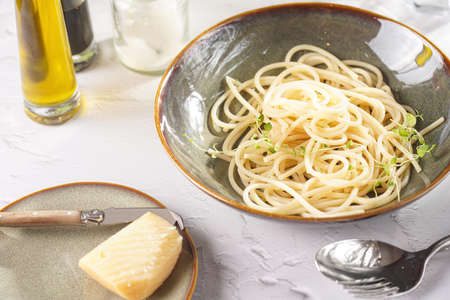 Italian spaghetti with parmesan cheese and fresh thyme in dark green bowl on white concrete surface, with olive oil and balsamic vinegar in the backの写真素材