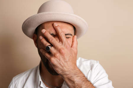 A young stylish caucasian man wearing a white shirt and a beige-colored hat covering his face with a...
