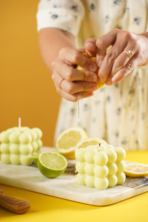 Female hands pressing lemon juice on a bright green bubble candle surrounded by lemon and lime halves, fresh thymeの写真素材