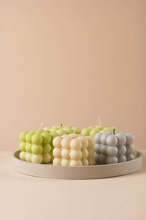 A pastel yellow, green and gray bubble candles on a concrete tray on a beige colored backgroundの写真素材