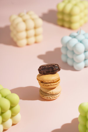 Three creamy, pink and chocolate macaron pastry stacked on top of each other surrounded by bright bubble candles on pink surfaceの写真素材