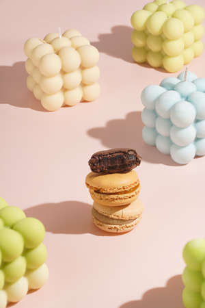 Three creamy, pink and chocolate macaron pastry stacked on top of each other surrounded by bright bubble candles on pink surfaceの写真素材
